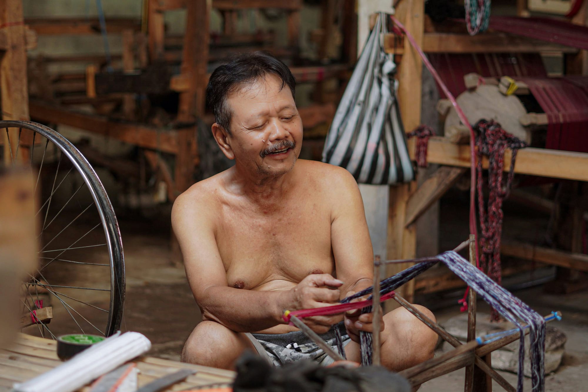 An Indonesian man prepares yarn for the hand-operated looms behind him.